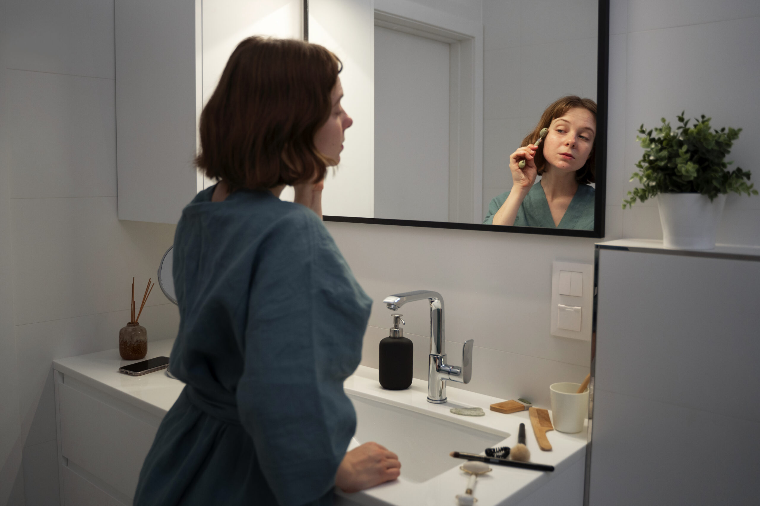 woman doing daily skincare routine in bright bathroom mirror