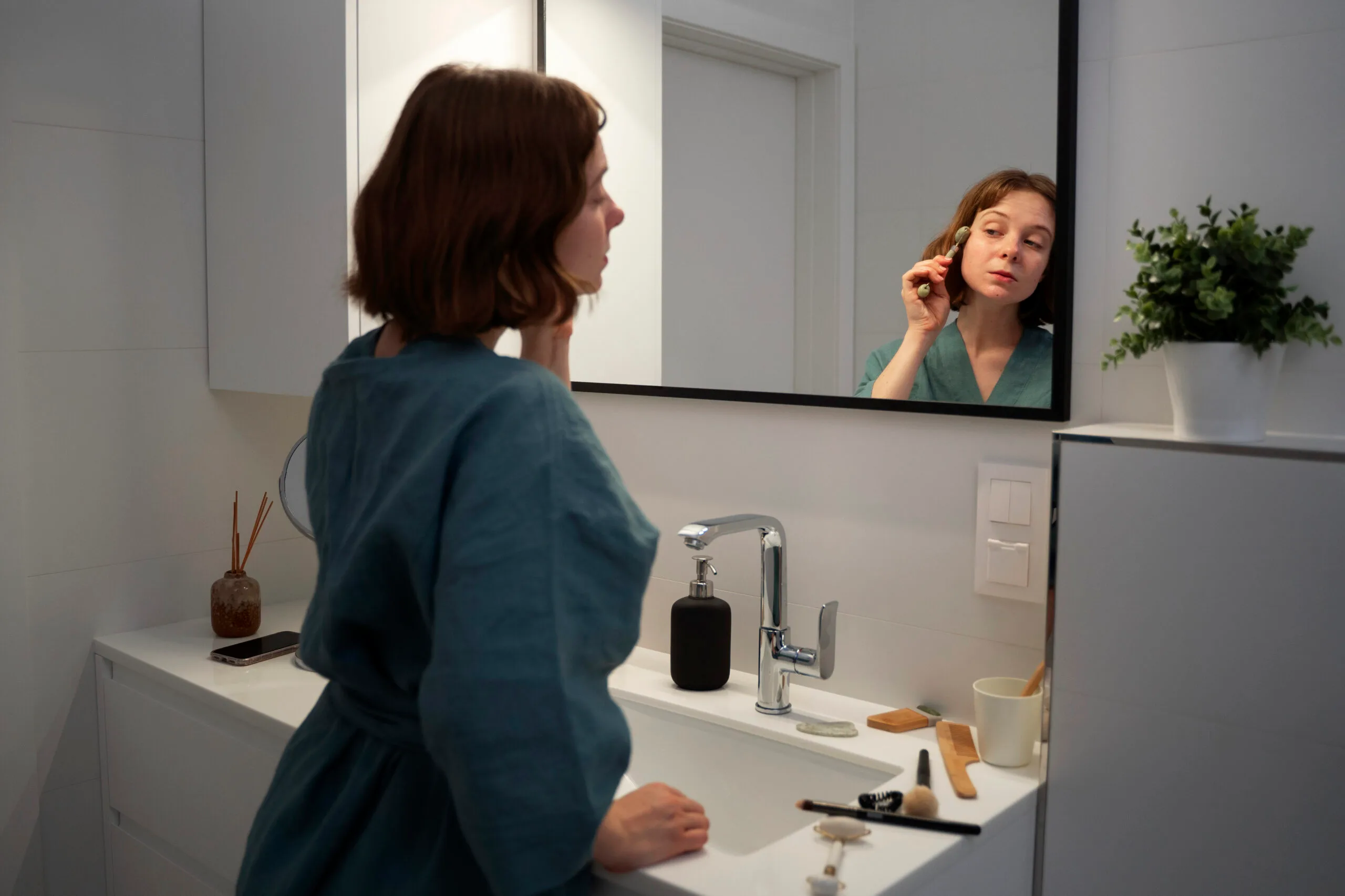 woman doing daily skincare routine in bright bathroom mirror